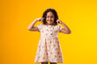 Kid girl covering ears over yellow background. Noise, stress and childhood concept
