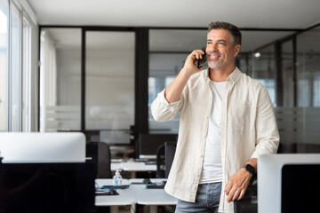 Wall Mural - Middle aged Latin or Indian businessman having call on smartphone with business partners or clients. Smiling mature Hispanic man in relaxing pose talking by mobile cellphone at work in modern office. 