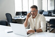 © Stock 4 You - Middle aged Latin or Indian businessman having call on smartphone with business partners or clients. Smiling mature Hispanic man sitting at table talking by mobile cellphone at workplace in office.