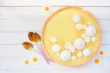 Poster - Spring lemon tart with white chocolate flowers and meringue. Top view table scene over a white wood background.