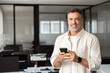 © Stock 4 You - Smiling at camera mature Latin businessman holding smartphone in office. Middle aged manager using cell phone mobile app. Digital technology application and solutions for business success development.