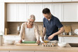 © fizkes - Happy elder mother and positive adult sun preparing bakery dessert for family dinner together, cooking breakfast, baking in home kitchen, rolling dough, beating eggs, enjoying culinary hobby