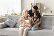 © fizkes - Three generations of happy family meeting at cozy home, resting on comfortable couch, hugging with love, laughing, enjoying family leisure, homey comfort. Dad embracing senior grandma and cute kid