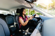 © Xavier Lorenzo - Young adult happy indian woman driving a car in the city. Rental car service concept