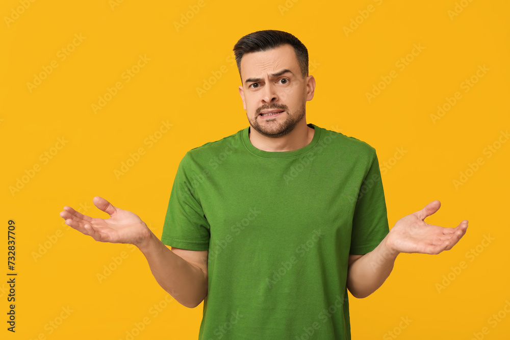 Handsome ashamed young man shrugging on yellow background