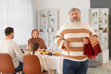 Wall Mural - Mature Muslim man with praying beads and mat at family dinner. Ramadan celebration