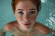 A woman with vibrant red hair and striking blue eyes is swimming and relaxing in a pool.