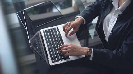 Wall Mural - Businesswoman working on laptop computer with digital tablet on office table, close up. Business woman typing, searching the information, surfing the internet via laptop, online working at office