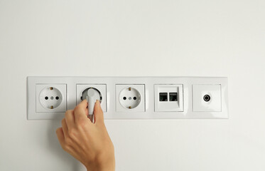 Wall Mural - Woman putting plug into socket indoors, closeup