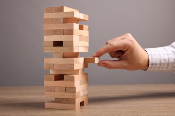 Poster - Playing Jenga. Man removing block from tower at wooden table against grey background, closeup