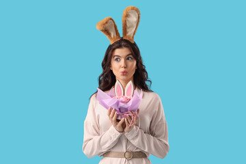 Sticker - Surprised beautiful woman in bunny ears with Easter cake on blue background