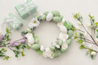 Leinwandbild Motiv Easter wreath with white flowers, eggs and butterflies on light background