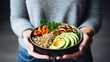 Healthy vegetarian dinner. Woman in jeans and warm sweater holding bowl with fresh salad, avocado, grains, beans, roasted vegetables, close-up. Superfood, clean eating.