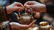 Two people are holding a beautifully crafted, small teapot adorned with intricate designs