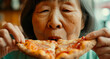 © Manu Prats - Senior Asian woman eating a slice of pizza