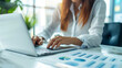 © Montipa - A focused businesswoman working on a laptop in an office setting, with financial charts and data analysis spreadsheets in front of her.
