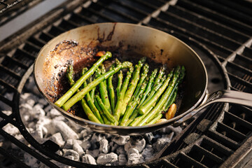 Wall Mural - Close-up of healthy frying green asparagus with butter and garlic on carbon steel frying pan. Outdoor BBQ grill