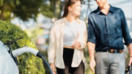 young couple recharge electric car battery from charging station in green city park in springtime. r