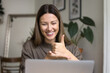 © fizkes - Cheerful hearing disability therapist talking on video conference call at laptop, speaking to patient, student, showing thumb up hand gesture on palm, smiling, laughing, enjoying communication