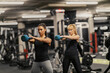 © dusanpetkovic1 - Portrait of two sportswomen swinging kettle bells in a gym and doing training together.