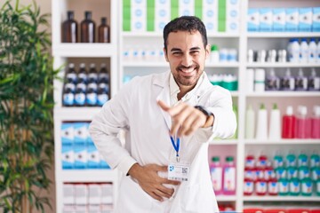 Poster - Handsome hispanic man working at pharmacy drugstore laughing at you, pointing finger to the camera with hand over body, shame expression