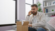 © Krakenimages.com - Young hispanic man speaking on the phone unpacking cardboard box at home