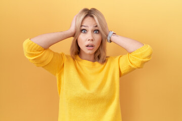 Sticker - Young caucasian woman wearing yellow sweater crazy and scared with hands on head, afraid and surprised of shock with open mouth