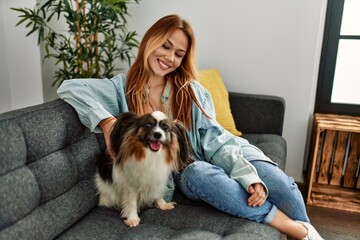 Wall Mural - Young caucasian woman smiling confident sitting on sofa with dog at home