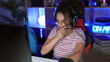 © Krakenimages.com - Curly-haired young hispanic woman wearing headphones in a dark gaming room with neon light