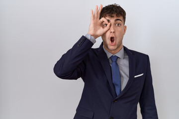 Canvas Print - Young hispanic business man wearing suit and tie doing ok gesture shocked with surprised face, eye looking through fingers. unbelieving expression.