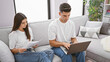 © Krakenimages.com - Man and woman focused on individual tasks with a laptop and papers in a modern living room setting.