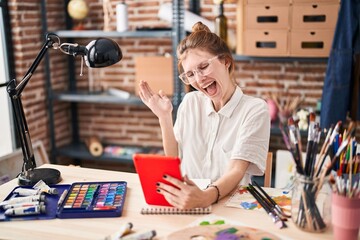 Wall Mural - Joyful young blonde artist celebrates triumph, looking at tablet screen with winner's smile in studio, radiating with confident happiness