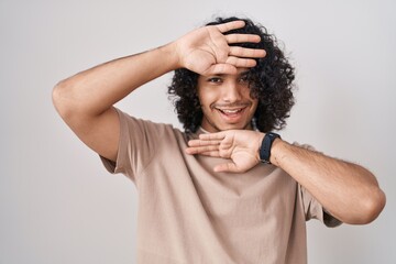 Poster - Hispanic man with curly hair standing over white background smiling cheerful playing peek a boo with hands showing face. surprised and exited