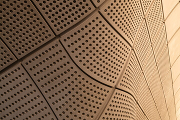 Curved and perforated contemporary wall panels bend around a structure in warm colours. Looks like porcelain or treated wood. Blank graphic design resource no people,  background wallpaper texture.