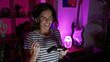 © Krakenimages.com - Epic win! dynamic young hispanic woman streamer, stunning with smile, celebrating gaming victory indoors. nailing the game with joystick control in her home-office gaming room at night.