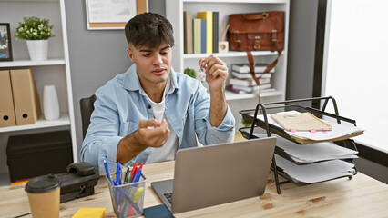 Sticker - Portrait of a young handsome hispanic man, a relaxed but serious business worker, immersed in online work on his laptop at the office desk, achieving success in his professional job indoors.