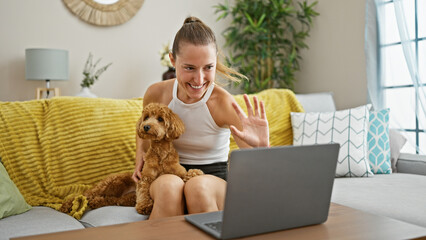 Wall Mural - Young caucasian woman with dog doing video call using laptop sitting on the sofa at home