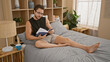 © Krakenimages.com - Young hispanic man wearing glasses reading book sitting on bed at bedroom