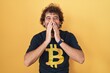Hispanic young man wearing bitcoin t shirt laughing and embarrassed giggle covering mouth with hands, gossip and scandal concept