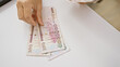 © Krakenimages.com - A woman's hands count saudi riyal banknotes at a white desk indoors reflecting finance and currency exchange.