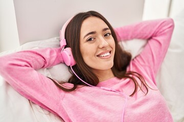 Wall Mural - Young beautiful hispanic woman listening to music lying on bed at bedroom