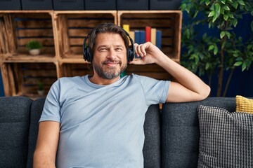 Wall Mural - Middle age man listening to music sitting on sofa at home