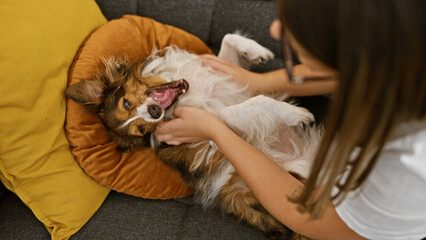 Canvas Print - A young woman enjoys leisure time with her fluffy dog on a cozy couch inside a tastefully decorated house.