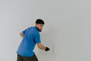 A young oriental man paints a wall with a roller.