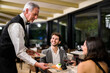 © Minerva Studio - Senior waiter serving young couple at elegant restaurant