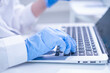 © Supapich - Closeup woman female scientist's hand blue protective glove using laptop for recording scientific medical experiment research from laboratory