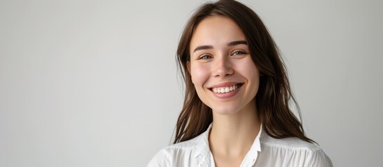 Wall Mural - Studio shot of a happy woman in a white blouse, smiling with teeth, gazing at the camera, isolated on a white background.