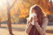 A woman with a runny nose in the park blows her nose into a napkin.