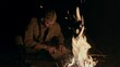 Soldier lighting a cigarette with a smouldering stick from a blazing campfire as he sits on the ground relaxing in the dark of night