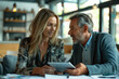 © Thiyanga - Energetic office dynamics: Middle-aged female executive engrossed in conversation with male colleague, collaborating on digital tablet, fostering a productive and cheerful work atmosphere.